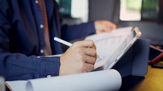 Businessman holding a paper document and cross-referencing data with a digital tablet at his office desk.