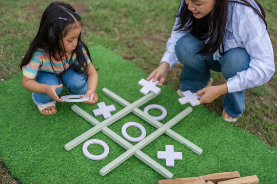 preschool child girl and mother playing tic tac toe game on green mat