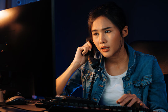 Young beautiful Asian creative woman calling on phone desk to customer or coworker explaining creator project's high profit while searching market analysis on pc at neon office at night. Stratagem.
