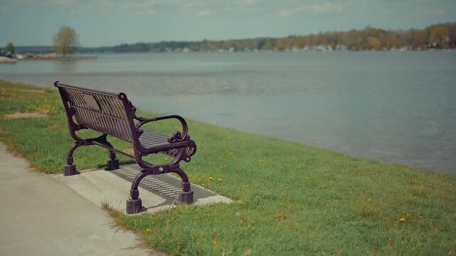 Bench on a water bank overlooking a lake with lake houses and trees in the background .