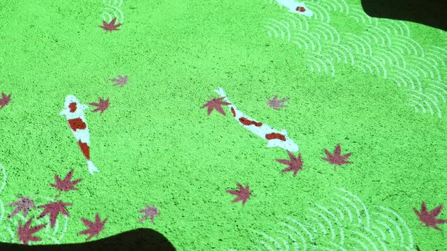 Projecting glowing carp fish and leaf patterns onto green sand in a