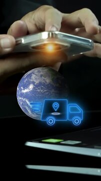 Businessman holding smartphone beside world globe model vertical shot with glowing delivery truck icon. International smart logistics tracking, freight transport, and cargo shipment idea concept.