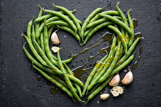 Fresh green beans arranged in heart shape on black slate with olive oil and garlic