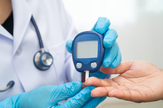 Asian doctor using digital glucose meter for check sample blood sugar level to treatment diabetes.