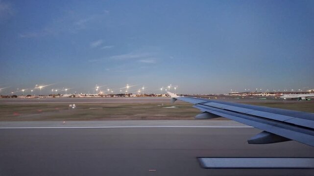 View from window shows airplane wing and taxiing aircraft at airport.