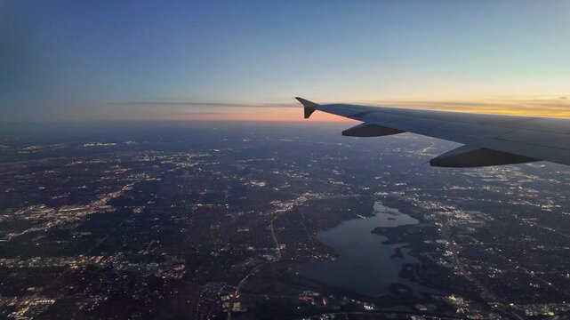 An airplane wing views a city illuminated at sunset.