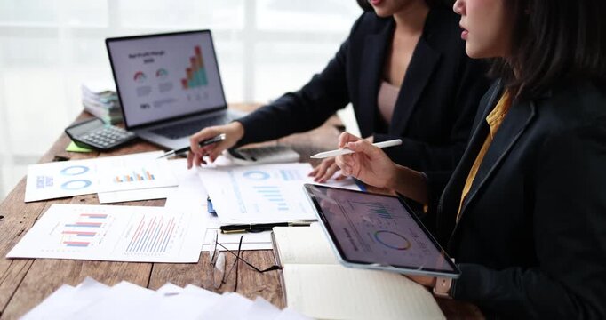 Two young businesswomen collaborating on financial data analysis, discussing corporate strategy and reviewing charts during a productive office meeting, focusing on growth and success
