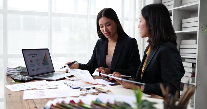 Two young businesswomen collaborating on financial data analysis, discussing corporate strategy and reviewing charts during a productive office meeting, focusing on growth and success
