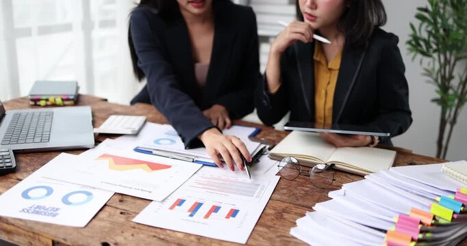 Two young businesswomen collaborating on financial data analysis, discussing corporate strategy and reviewing charts during a productive office meeting, focusing on growth and success