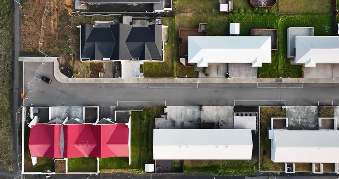 Top-down drone view over Grindavik, Iceland, showing a quiet residential street lined with modern homes, red and white roofs, private yards and neat suburban plots.