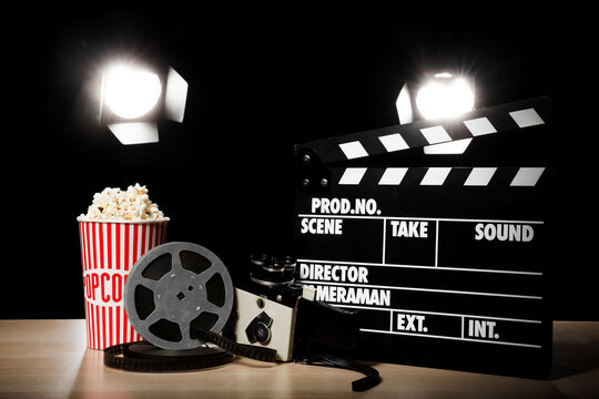 Film production and cinema industry, movie clapperboard with vintage camera and popcorn bucket on a wooden table under professional studio lighting