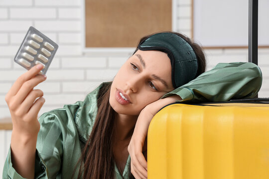 Jet lag and travel fatigue, tired woman with sleep mask holding medication pills near suitcase for health issues during business trip or vacation
