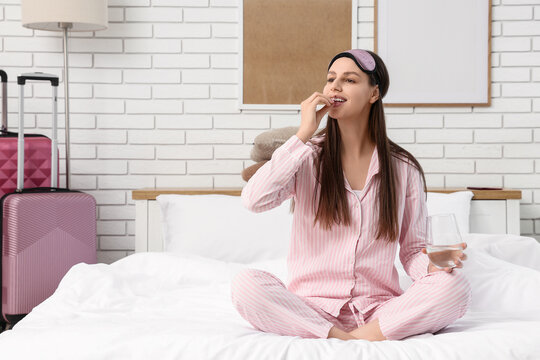 Sleep aid and insomnia treatment, young woman taking medication with water in hotel room before bed to manage jet lag and travel fatigue