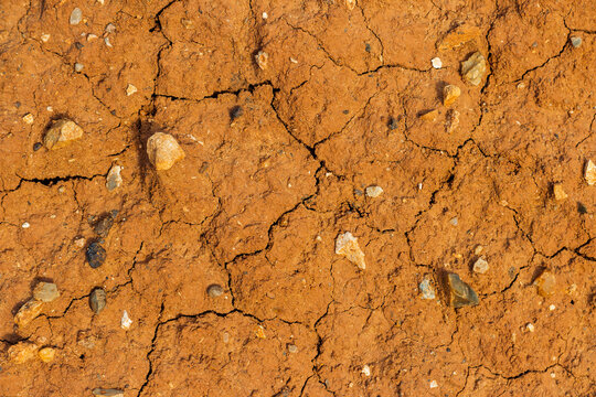 Top view of parched arid earth with deep cracks and scattered pebbles, showing dry orange soil texture scorched by heat under the bright sun in a desert landscape