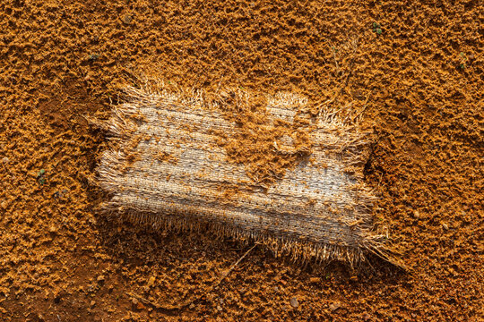 Tattered old fabric piece lying abandoned on coarse desert sand with rough textures creating a moody contrast between the decaying textile and the dry gritty earthen ground