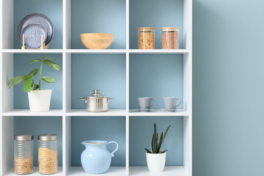 Home organization and kitchen storage, minimalist interior design with pantry staples and decorative plants on white shelving unit against blue wall