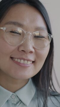 Close-up slow motion portrait of cheerful Asian lady smiling looking at camera against blurred apartment background. Good mood and people concept.