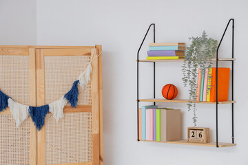 Fototapeta premium Bookshelf with ball and plant on light wall in childrens room