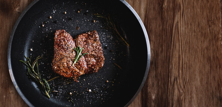 Grilled beef steak in frying pan, on wood texture background