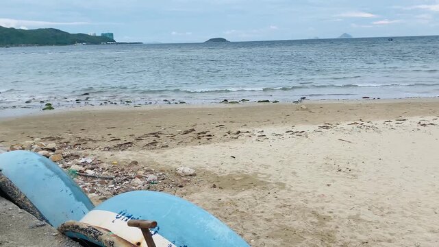 Wide landscape of a tropical sandy beach in Nha Trang, Vietnam with traditional Vietnamese round coracle basket boats, sea waves, and hills in the distance.
