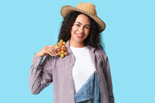 Happy young African-American woman in wicker hat with sweet ripe grapes on blue background