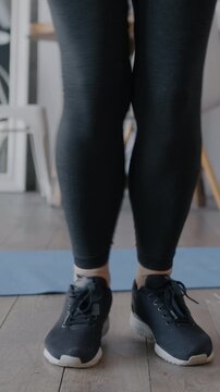 Low shot of female legs wearing leggings and sneakers skipping with jumping rope while woman doing sports and home. Active lifestyle and sportswear concept.