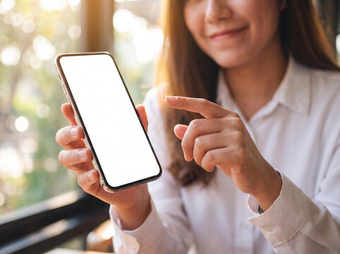 A woman holding a blank white screen smartphone and pointing at it, with a blurred background.