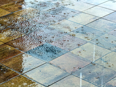 raindrops splashing on wet pavement tiles and creating ripples with bubbles.