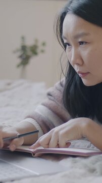 Slow motion of Asian entrepreneur working with laptop and writing in notebook planning business in bedroom at home. Computing and businessperson concept.