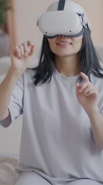 Slow motion of young lady wearing virtual reality glasses gesturing sitting on bed in luxury apartment. Modern technology and lifestyle concept.
