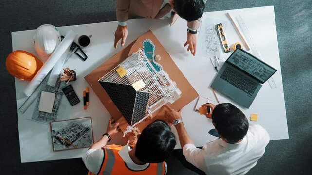 Top aerial view of architect engineer team stick sticky notes on house model while working together to design building construction at table with laptop, safety helmet and project plan. Alimentation.