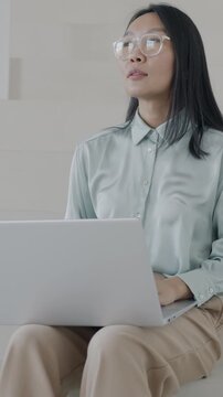 Beautiful Asian lady working with laptop typing sitting on stairs in stylish luxury house. Computer and elegant interior concept.