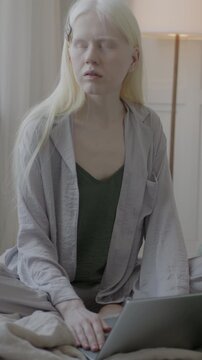 Slow motion of pensive albino woman in pajamas working with laptop thinking sitting in bed in luxury house. Modern technology and people concept.