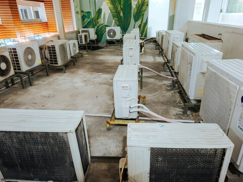 An outdoor service area filled with multiple air conditioner compressor units mounted on metal frames against a wall with a leaf pattern