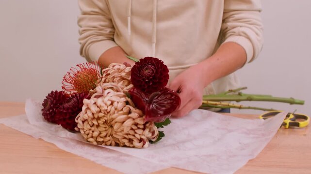 Bloom composition. Floral workshop. Unrecognizable professional female florist preparing paper on table for chrysanthemum flowers.
