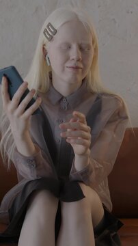 Beautiful albino woman making mobile phone call using wireless earphones and smartphone talking sitting on couch in stylish house. Communication and people concept.
