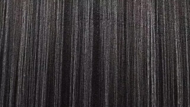 Dark waterfall surface with continuous streams of water creating a striped natural pattern. Moody background for motion, texture and environment themes. Modern fountain wall in Kyoto, Japan.