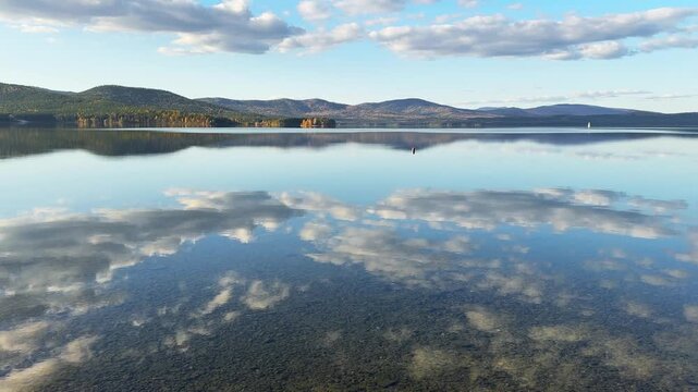 Autumn mountains and sky with clouds are reflected in the water. Beautiful autumn landscape. Turgoyak lake in Southern Urals, Russia.
