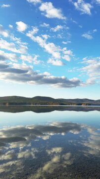 Autumn mountains and sky with clouds are reflected in the water. Beautiful autumn landscape. Turgoyak lake in Southern Urals, Russia. Vertical video
