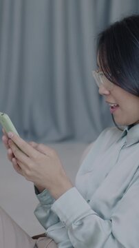 Slow motion of Asian lady using smartphone enjoying social media content and laughing in luxury apartment. Internet communication and people concept.