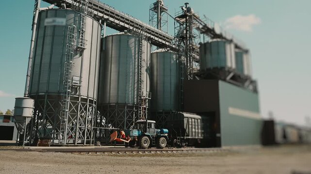 Modern grain elevator complex with large metal storage silos, conveyor systems and agricultural machinery used for bulk crop storage and handling.