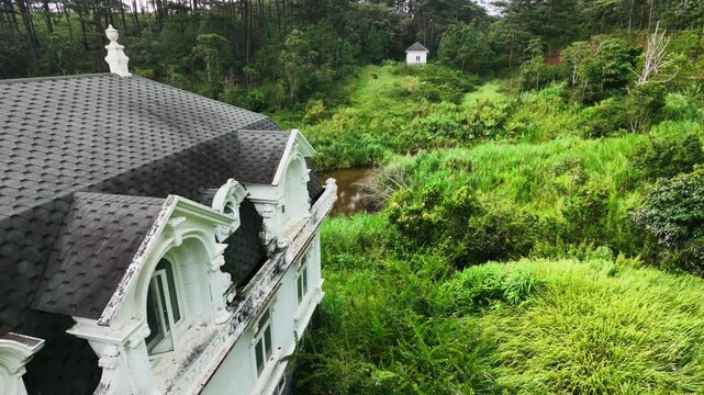 Aerial view abandoned white house  over river winding through lush green forest with distant gazebo