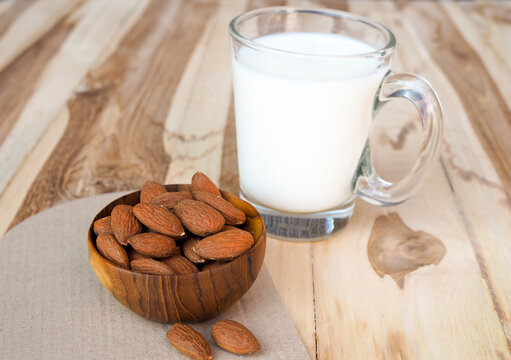 Glass of fresh almond milk with raw almonds in wooden bowl on wooden background.