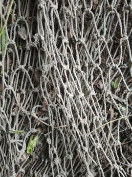 Close-up of grungy woven rope net texture resting on natural ground background.