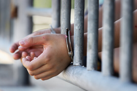 Close-up of hands holding prison bars in a detention facility setting