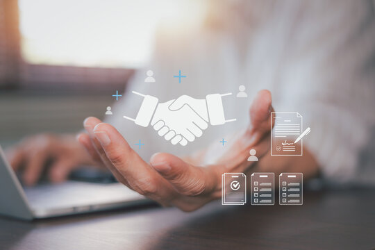Businessman hand presenting virtual handshake hologram with contract documents. Concept of digital partnership, online agreement, business deal, trust, and corporate teamwork collaboration.