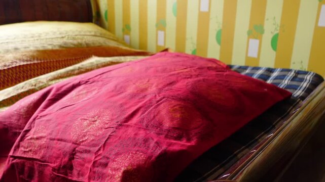 Person spreads red and gold decorative bedsheet over blue checkered mattress in bedroom.