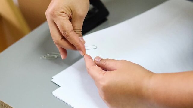 Close up of person hands attaching metal paper clips to stack of white documents on office desk.