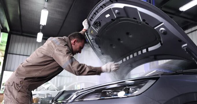 Startled mechanic reacts as smoke rises from beneath an open car hood in an automotive repair garage. The scene illustrates an unexpected vehicle malfunction, urgent inspection.