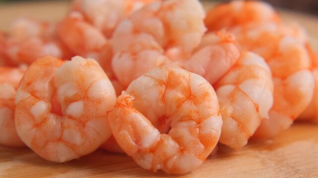 Pile of cooked shrimp with orange shells on wooden cutting board macro view.
